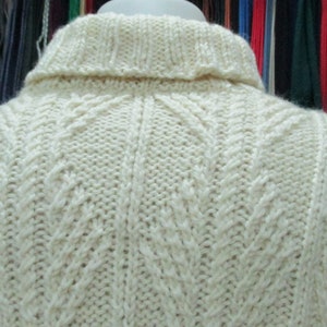 Puede incluir: Un su&eacute;ter de punto blanco con un patr&oacute;n de punto de cable. El su&eacute;ter tiene un cuello alto y est&aacute; hecho de un material suave y c&aacute;lido.