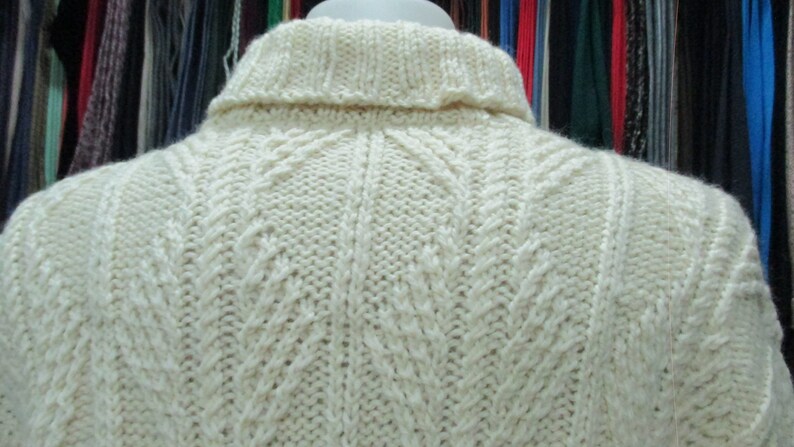 Puede incluir: Un su&eacute;ter de punto blanco con un patr&oacute;n de punto de cable. El su&eacute;ter tiene un cuello alto y est&aacute; hecho de un material suave y c&aacute;lido.