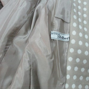 May include: A beige jacket with a white polka dot pattern. The jacket lining is a light beige color. The label on the jacket reads "Moda Stylbert".