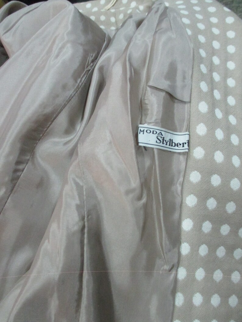 May include: A beige jacket with a white polka dot pattern. The jacket lining is a light beige color. The label on the jacket reads "Moda Stylbert".