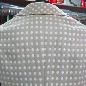 May include: A beige blazer with a white polka dot pattern. The blazer has a classic style with a notched collar and a single-breasted closure.
