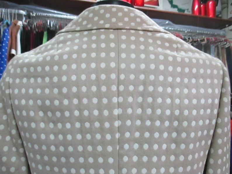 May include: A beige blazer with a white polka dot pattern. The blazer has a classic style with a notched collar and a single-breasted closure.