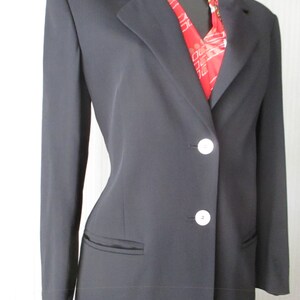 May include: A black blazer with a notched lapel and two white buttons. The blazer has two front pockets and is worn over a red patterned scarf. The blazer is displayed on a black mannequin.