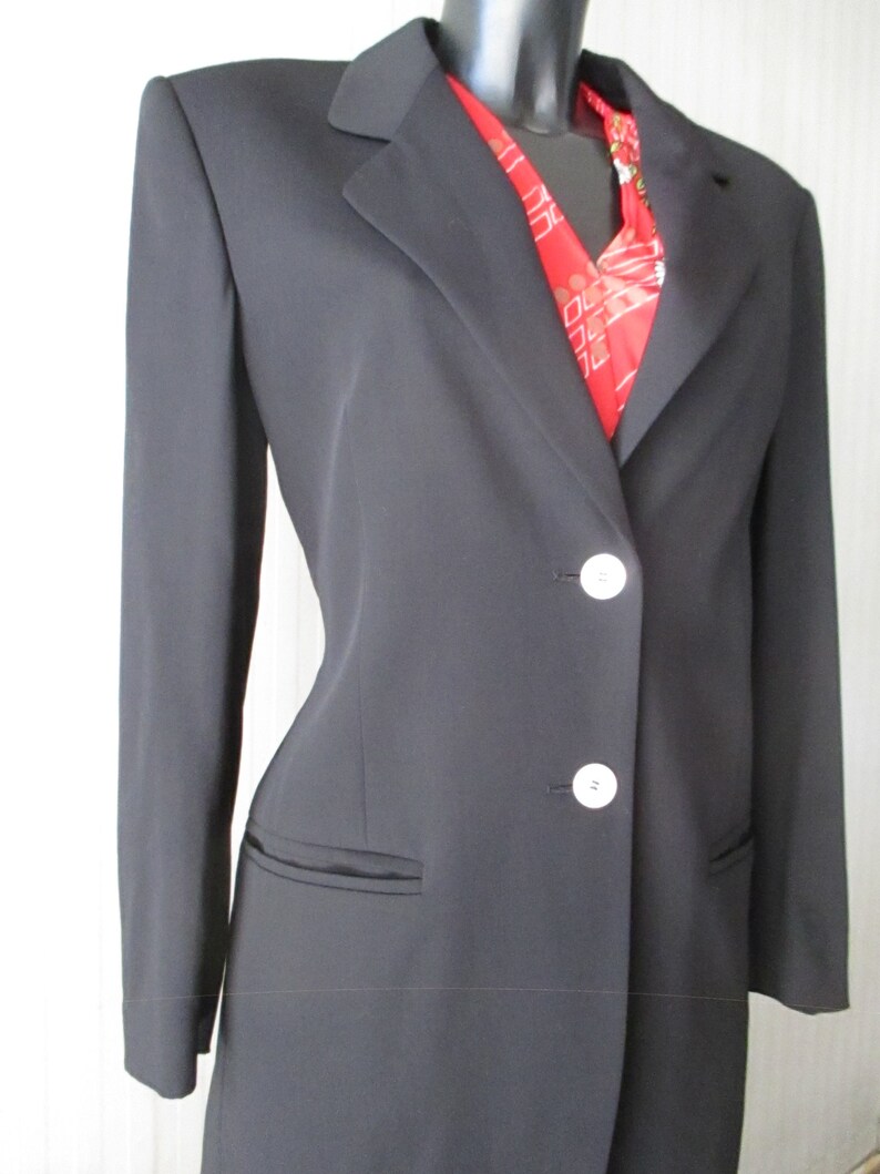 May include: A black blazer with a notched lapel and two white buttons. The blazer has two front pockets and is worn over a red patterned scarf. The blazer is displayed on a black mannequin.