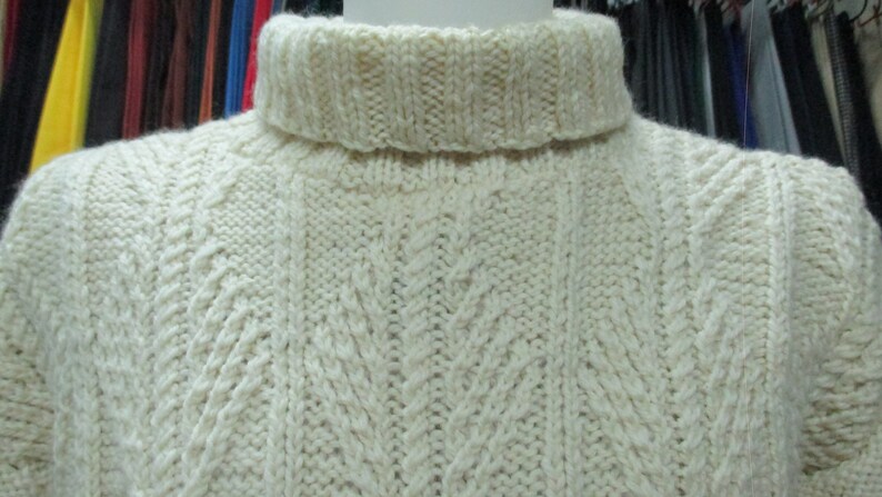 Puede incluir: Un su&eacute;ter de cuello alto de punto blanco con un patr&oacute;n de punto de cable.