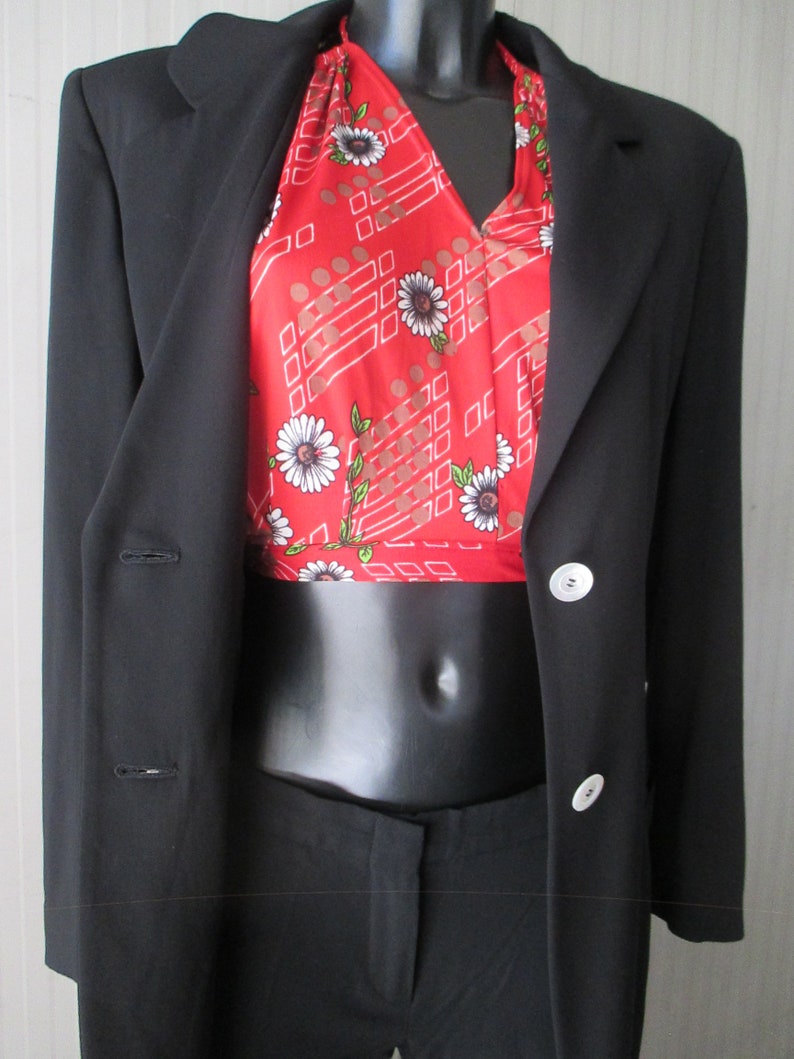 May include: A black blazer with a red halter top featuring a white floral pattern and geometric design. The outfit includes black pants, creating a classic and stylish ensemble.