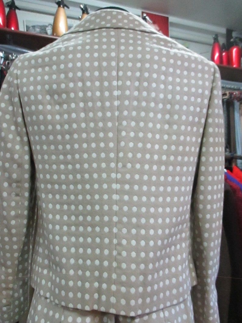 May include: A beige blazer with a white polka dot pattern. The blazer is cropped and has a collar.