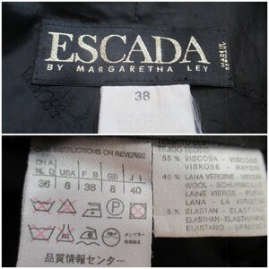 May include: Close-up of a black Escada label with gold lettering, reading "ESCADA BY MARGARETHA LEY MADE IN GERMANY." Below, a white tag displays the size "38" and fabric content details. Additional care symbols are also visible.