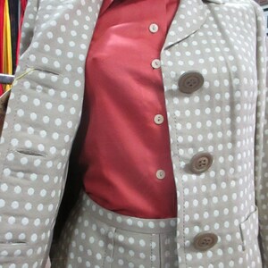May include: A beige blazer with white polka dots and a red button-down shirt. The blazer has a collar and four buttons down the front. The shirt has a collar and five buttons down the front.