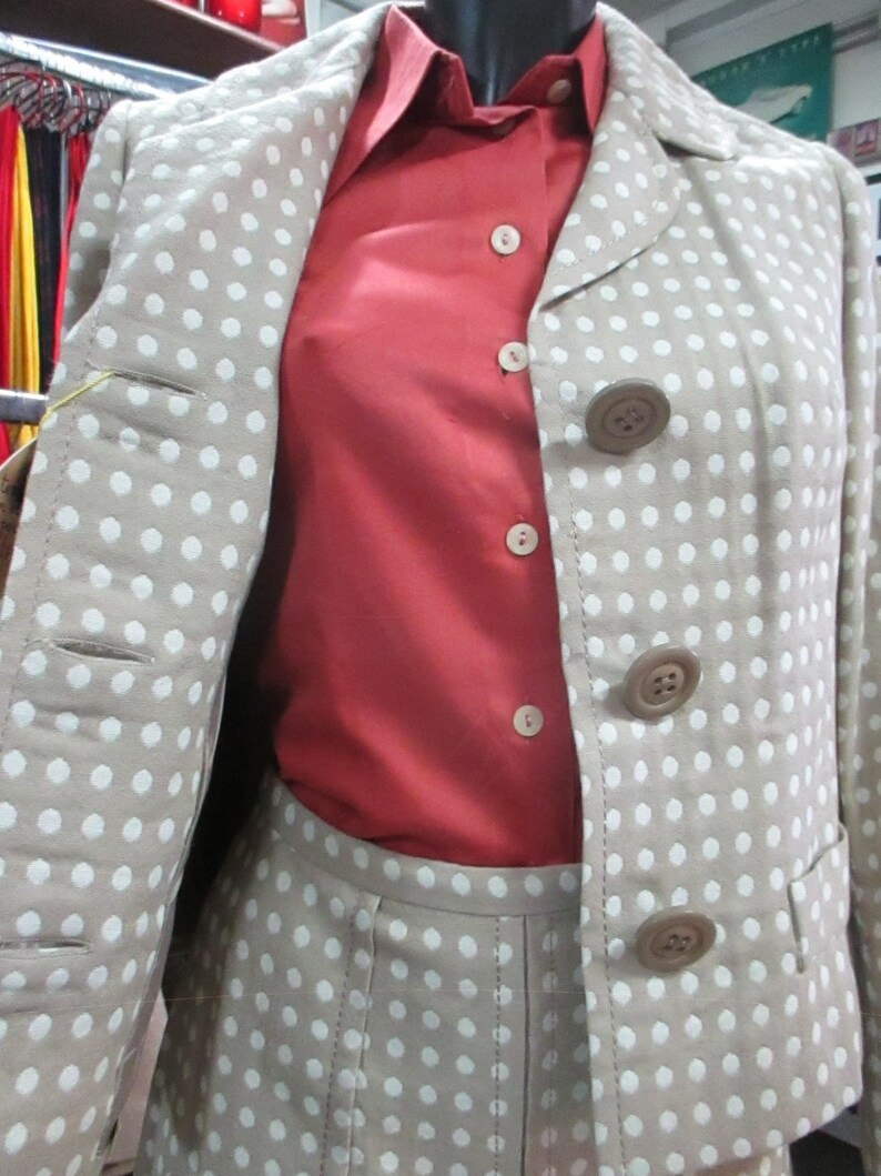May include: A beige blazer with white polka dots and a red button-down shirt. The blazer has a collar and four buttons down the front. The shirt has a collar and five buttons down the front.