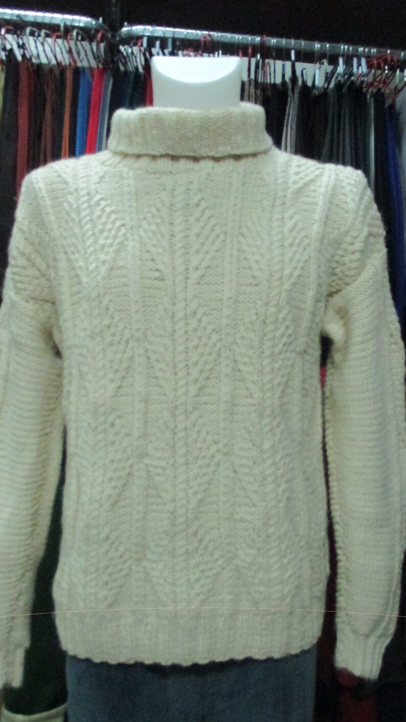 Puede incluir: Un su&eacute;ter de punto de color crema con cuello alto y un patr&oacute;n de punto de cable.