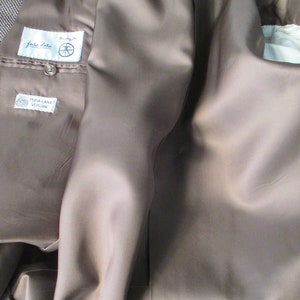 May include: The inside of a brown blazer with a brown satin lining. The label reads "Fiore Fiore" and "Pura Lana Vergine".