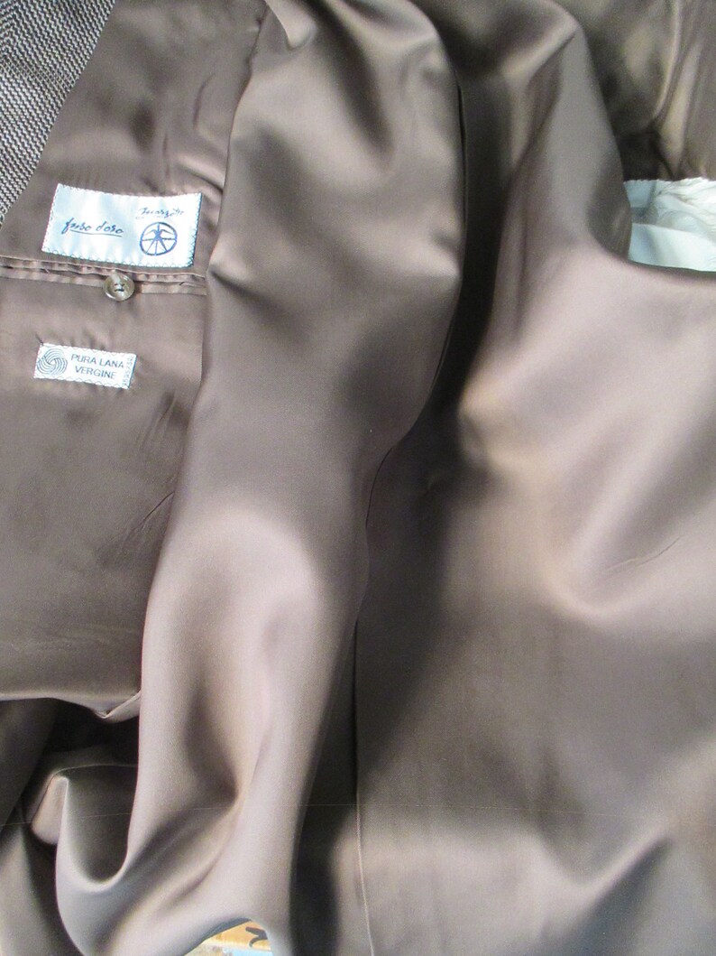 May include: The inside of a brown blazer with a brown satin lining. The label reads "Fiore Fiore" and "Pura Lana Vergine".