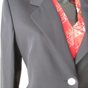 May include: A black blazer with a single white button closure. A red scarf with a white and floral pattern is visible beneath the lapel. The blazer has a classic notched collar and a tailored fit.