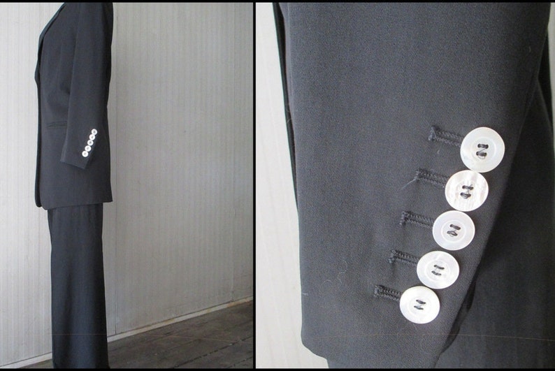 May include: A dark navy blue suit, featuring a tailored blazer with white buttons on the sleeve and matching trousers. The suit is displayed against a neutral background, showcasing its classic design and professional style.