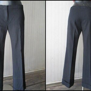 May include: Black dress pants with a slight flare at the hem. The pants have a classic design with a button and zipper closure, and a tailored fit. The cuffs are turned up. The pants are displayed on a mannequin.
