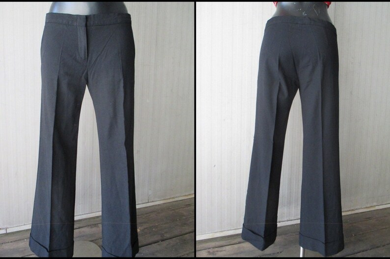 May include: Black dress pants with a slight flare at the hem. The pants have a classic design with a button and zipper closure, and a tailored fit. The cuffs are turned up. The pants are displayed on a mannequin.