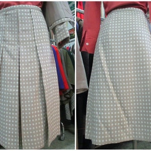 May include: A beige skirt with white polka dots and pleats. The skirt is knee-length and has a simple design.