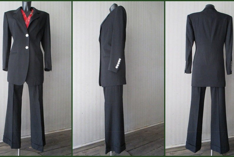 May include: A black suit with a long jacket and flared pants. The jacket has two white buttons and a red patterned shirt is visible underneath. The suit is displayed on a mannequin. The pants have a cuff.