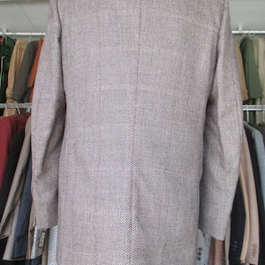 May include: A brown and white herringbone patterned suit jacket. The jacket has a single-breasted closure and long sleeves.