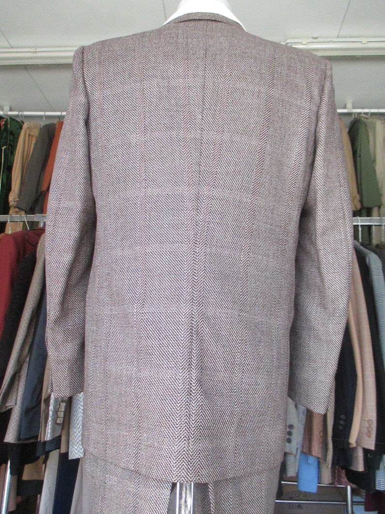 May include: A brown and white herringbone patterned suit jacket. The jacket has a single-breasted closure and long sleeves.