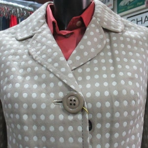 May include: A beige polka dot jacket with a red collared shirt underneath. The jacket has a single button closure.