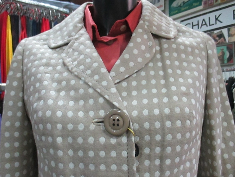 May include: A beige polka dot jacket with a red collared shirt underneath. The jacket has a single button closure.