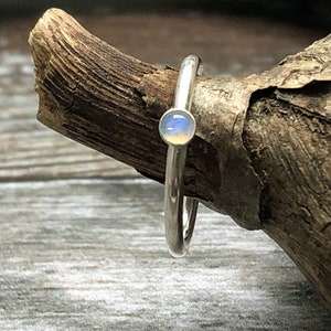 May include: A silver ring with a small, round, iridescent opal gemstone.