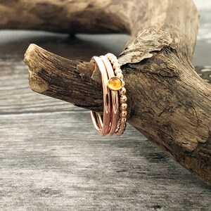 May include: A set of three rose gold rings, one with a small yellow gemstone, on a piece of driftwood.