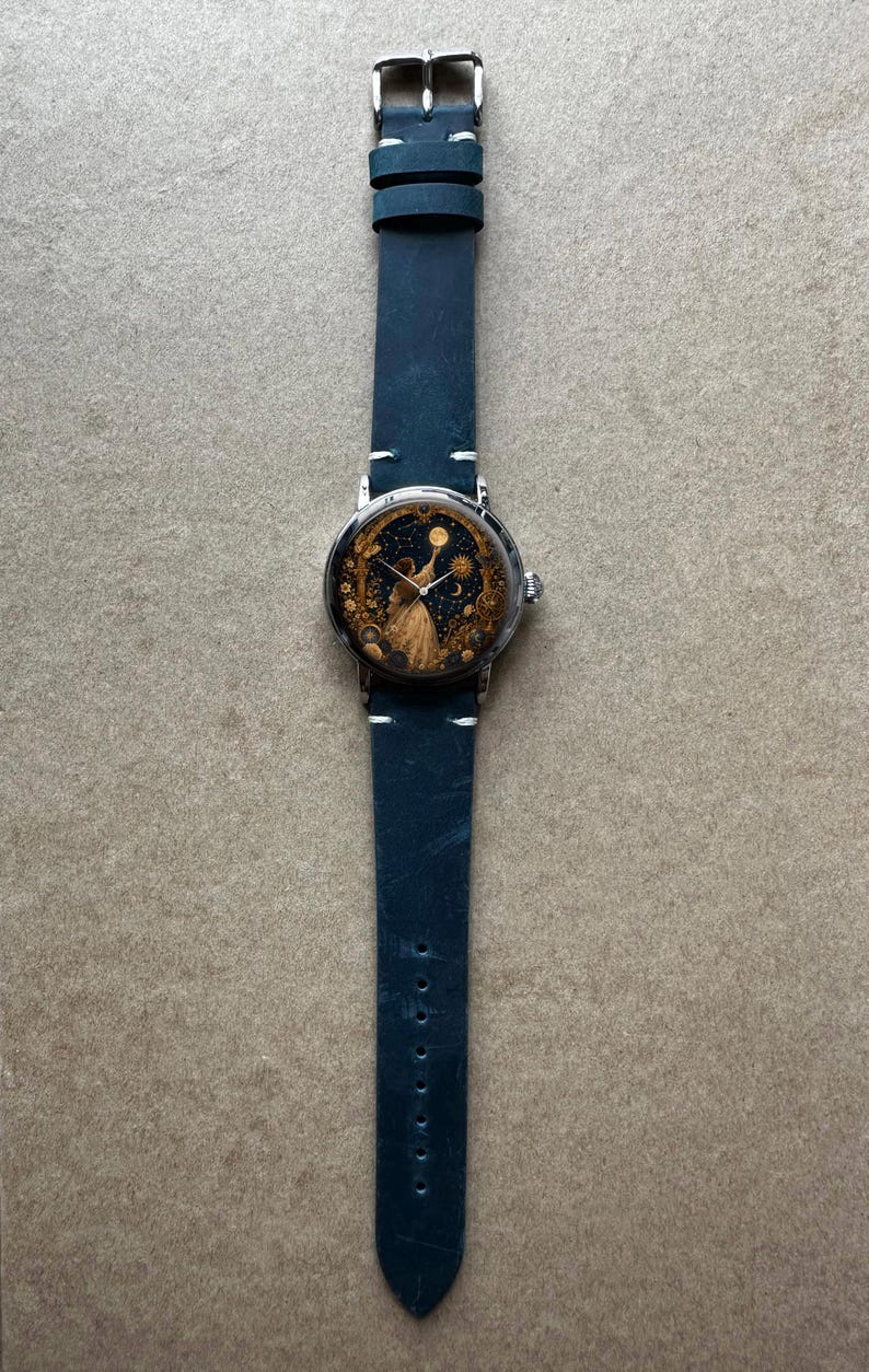 May include: A silver-toned wristwatch with a dark blue leather strap. The watch face features a celestial design with a figure reaching for the moon and stars. The strap is approximately 23 cm long.