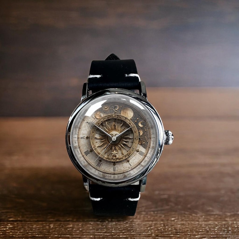 Puede incluir: Un reloj de pulsera redondo con una correa de cuero negro y costuras blancas. La esfera del reloj presenta un dise&ntilde;o de sol y luna con n&uacute;meros romanos. El reloj tiene una caja plateada y una cubierta de cristal transparente.