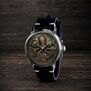 May include: A round wristwatch with a black leather band. The watch face features a detailed illustration of an octopus with gears and Roman numerals. The watch has a silver-colored case and a black leather strap.