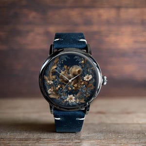 May include: A round wristwatch with a dark blue leather strap. The watch face displays a detailed illustration of a squirrel surrounded by foliage and flowers in brown, beige, and blue. The watch case is black.