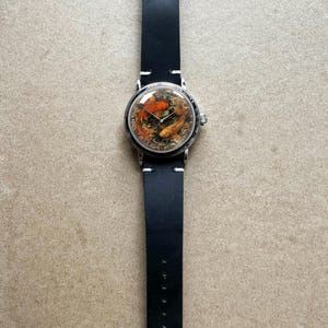 May include: A round wristwatch with a silver case and a black leather band. The watch face features a detailed image of koi fish in shades of orange and gold. The band is approximately 1 inch wide.