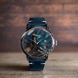 Könnte beinhalten: Runde Armbanduhr mit detailliertem Seelandschaftsdesign mit einem Leuchtturm unter den Nordlichtern. Die Uhr hat ein schwarzes Gehäuse, ein blaues Lederarmband und eine silberne Krone. Das Zifferblatt enthält eine Windrose und ein Segelboot.