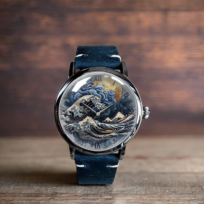 May include: A round wristwatch with a black case and a blue leather band. The watch face features a detailed illustration of a wave with a full moon. The watch has silver hands and Roman numeral hour markers.
