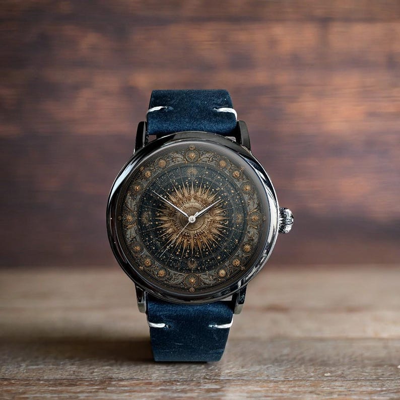 May include: A black wristwatch with a celestial design on the face and a blue leather band. The watch face features a detailed sunburst pattern with gold accents. The band is approximately 0.75 inches wide.