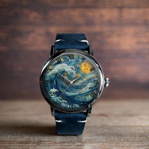 May include: A wristwatch with a black case and a blue suede strap. The watch face displays a painting of a wave, moon, and stars in blue and yellow hues. The watch has silver hands and Roman numeral hour markers.