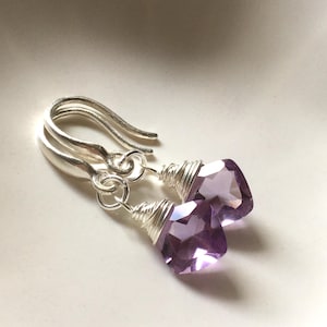 May include: A pair of drop earrings featuring faceted, light purple, square-cut gemstones. Each stone is secured with silver-coloured wire wrapping at the top, connected to a curved silver-coloured ear wire hook for a simple, dangling design.