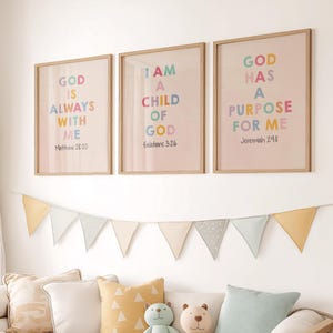May include: Three framed prints with inspirational quotes about God. The prints are in a light pink colour with colourful text. The quotes are "God is always with me", "I am a child of God", and "God has a purpose for me".