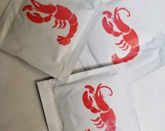 May include: Three white paper packets with a red lobster design printed on each. The lobster is facing right on the left packet, facing left on the right packet, and facing right on the center packet.