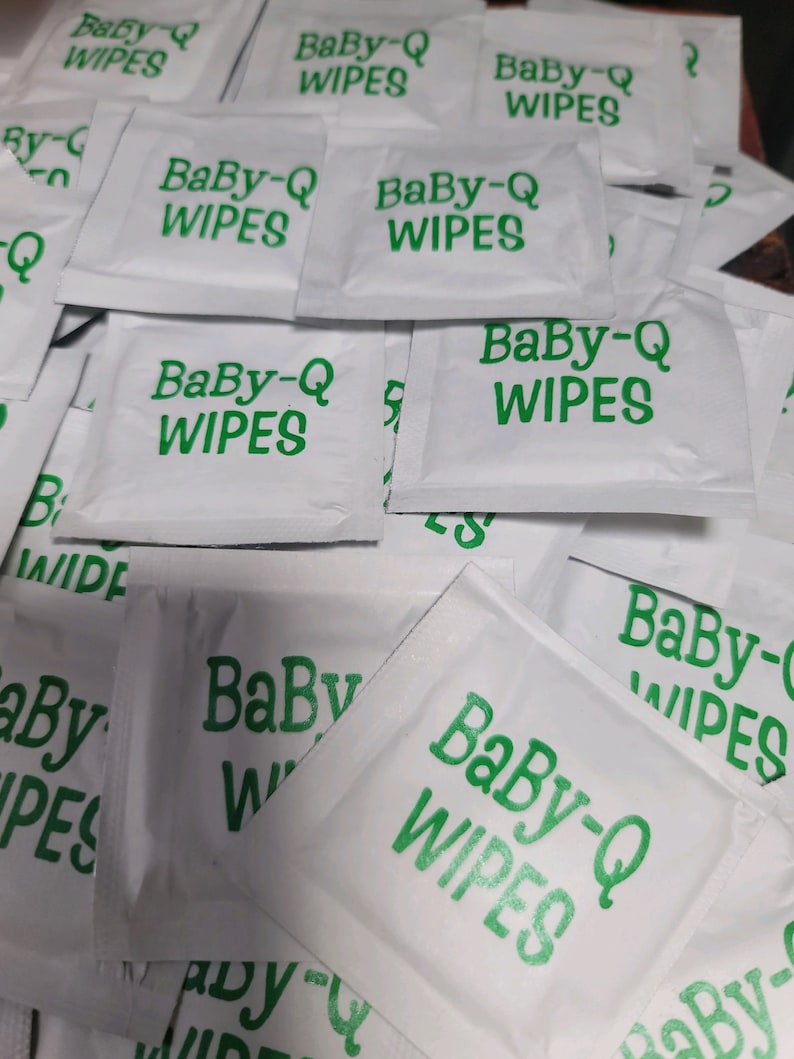 May include: A pile of white Baby-Q wipes with green text. The wipes are individually packaged in small, rectangular pouches.