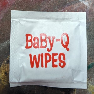 May include: A white package with red text that reads "Baby-Q Wipes".