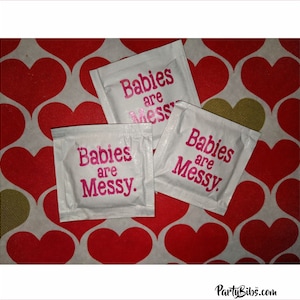 May include: Three white sugar packets with the text "Babies are Messy" printed in pink on each packet. The packets are on a red and gold heart patterned background.