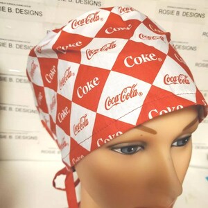 Peut inclure: Un bonnet de chirurgien à carreaux rouges et blancs avec le logo Coca-Cola et le mot "Coke". Le bonnet a une attache à l'arrière. Conçu par Rosie B. Designs.