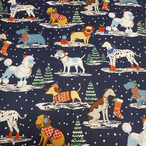 Op de afbeelding: Een donkerblauwe stof met een herhalend patroon van honden die winterkleding en hoeden dragen. De honden staan in verschillende poses, waaronder zittend, staand en rennend. Er zijn ook kleine groene kerstboompjes en witte sneeuwvlokken verspreid over het patroon.