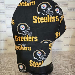 May include: Black and yellow fabric welding cap with a repeated pattern of the Pittsburgh Steelers logo. The logo features a football helmet with the team's name and a star.