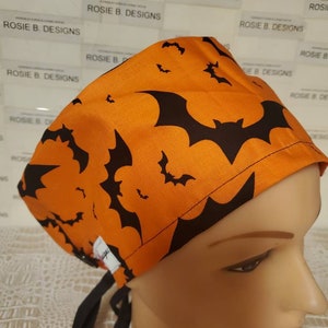 May include: Orange surgical scrub hat with a black bat pattern. The hat has black ties.