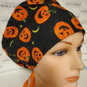 May include: Black scrub hat with a Halloween pumpkin print. The hat has orange ties and a black background with orange pumpkins and white stars.
