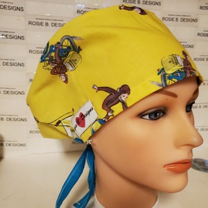 May include: Yellow surgical scrub hat with a blue tie. The hat has a repeating pattern of monkeys riding bicycles with a red heart and the text "Rosie B. Designs".